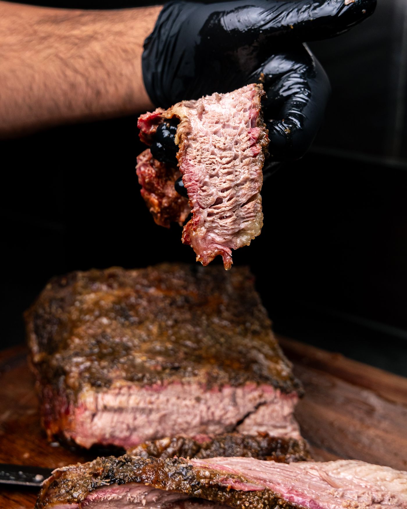 Slice of smoked brisket with a pink smoke ring held above the whole brisket